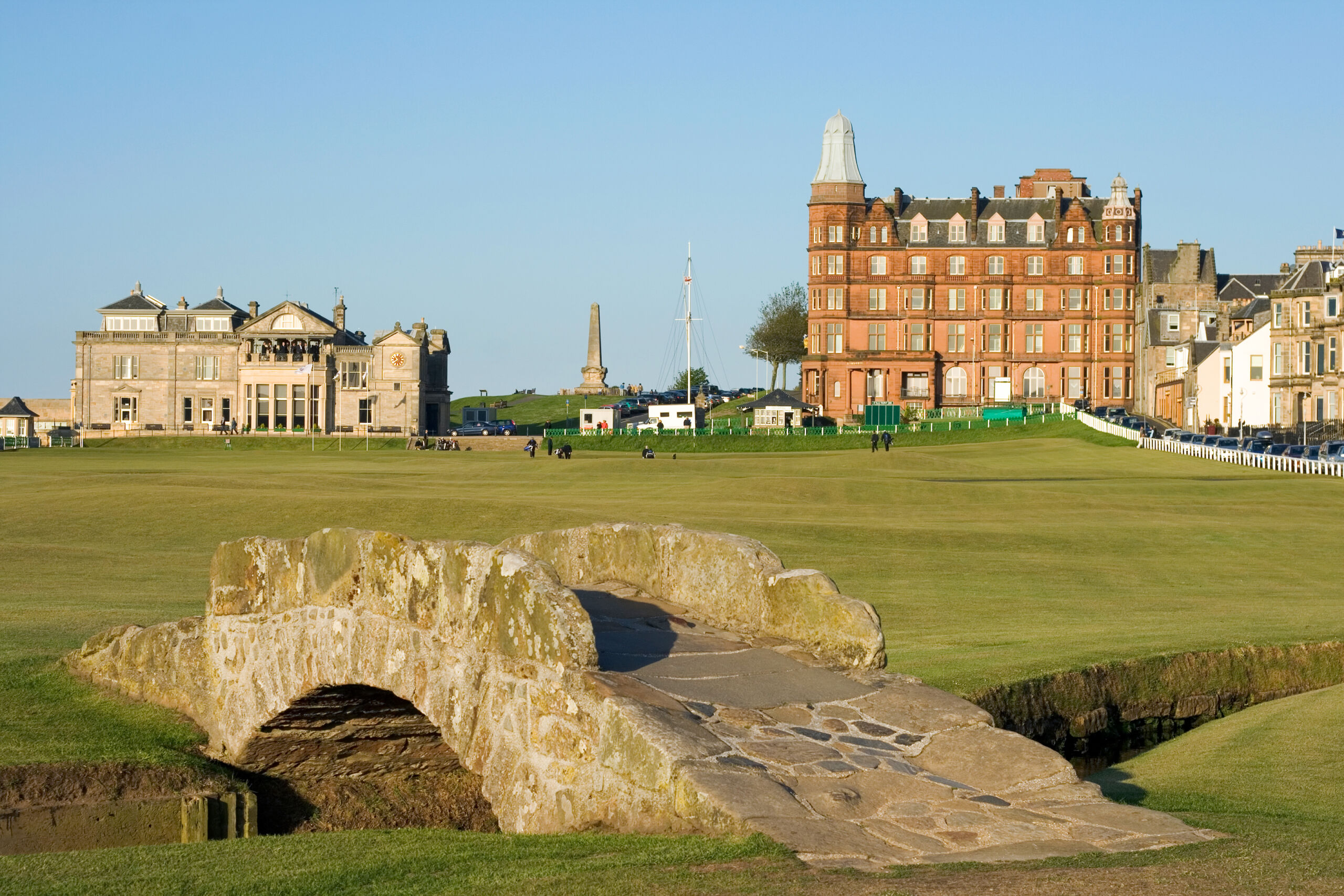 A stone bridge over a valley with a golf course and buildings in the background