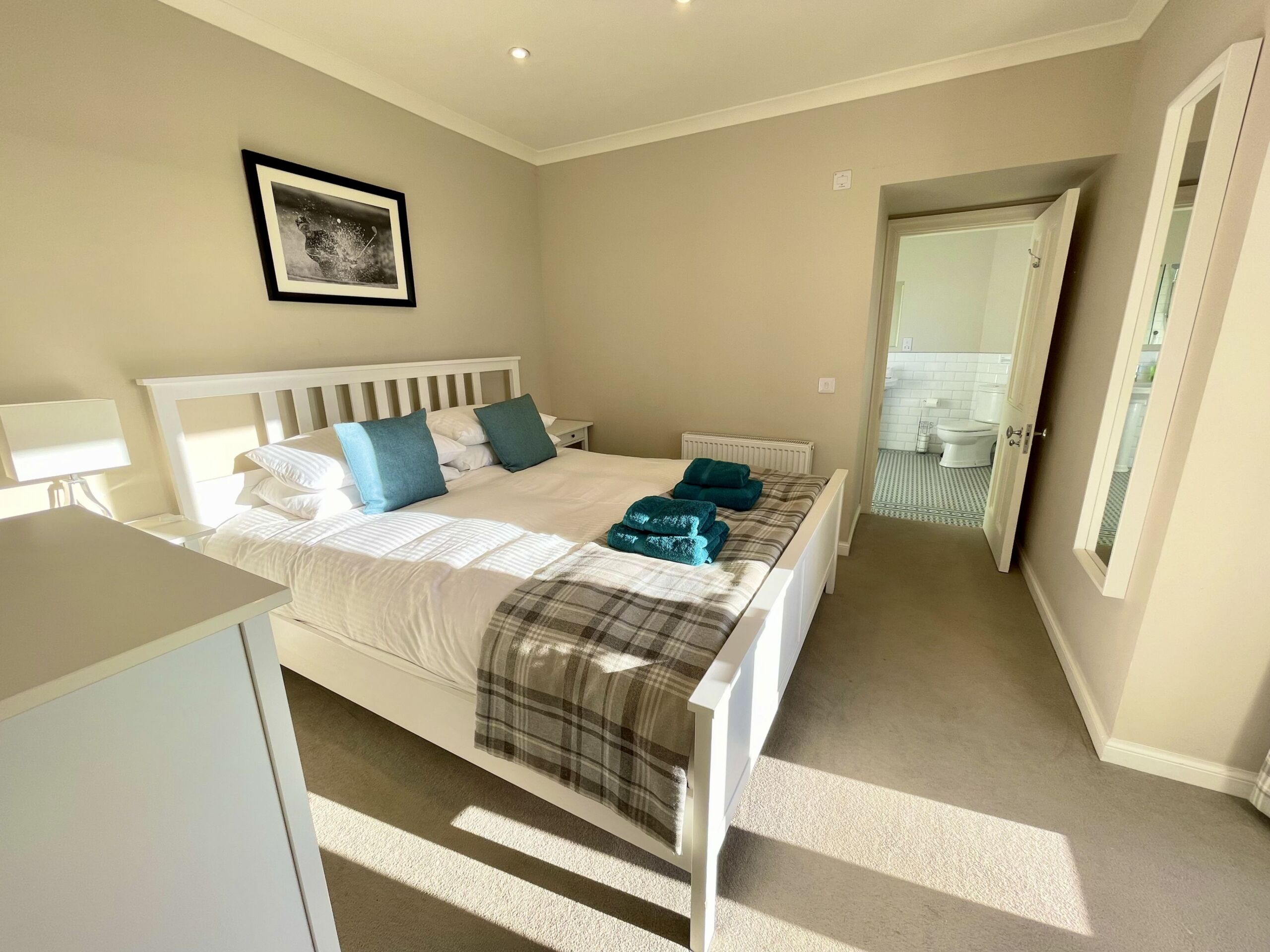 A bedroom with a white bed, blue pillows and tartan rug