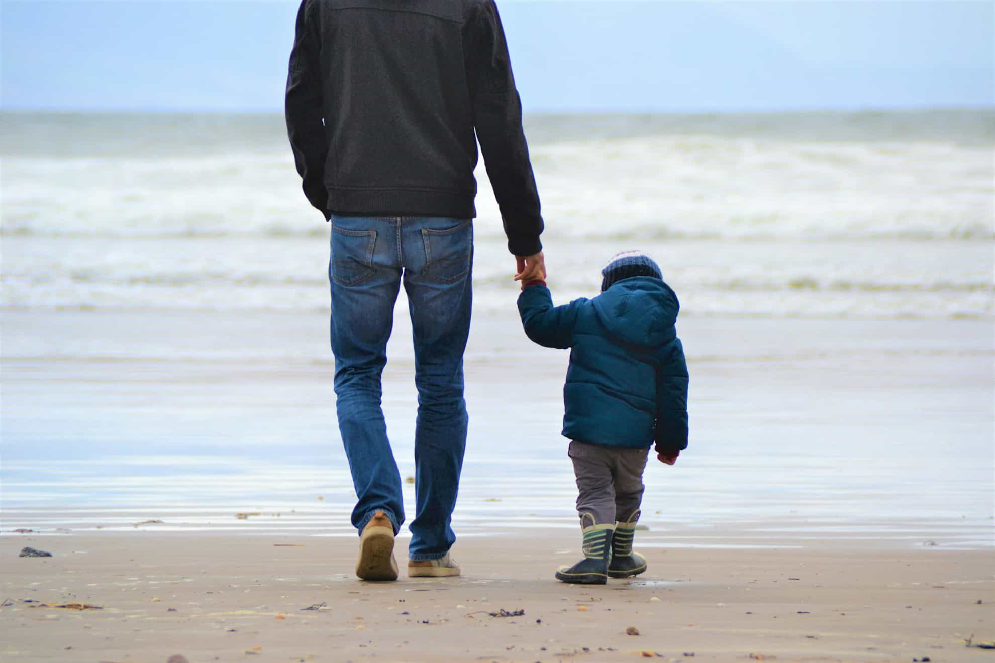 A man and a toddler walking on a beach